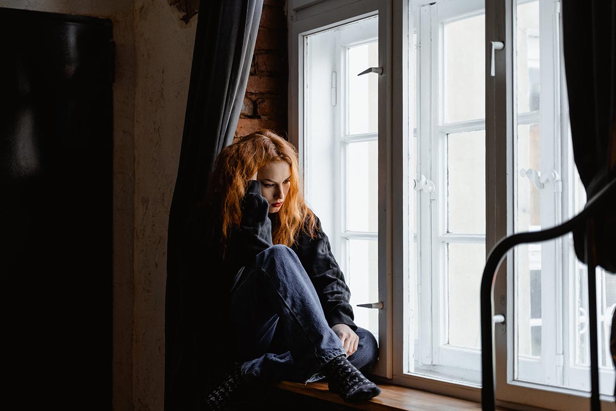 a woman sitting near the window thinking about how to avoid Isolating in Recovery